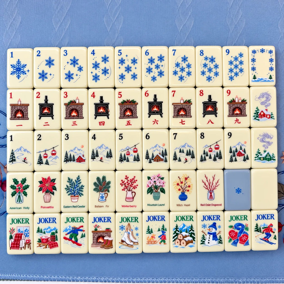 Ivory Snowfall Reverie Mahjong tiles with snowflakes, fireplaces and winter artwork on blue fabric